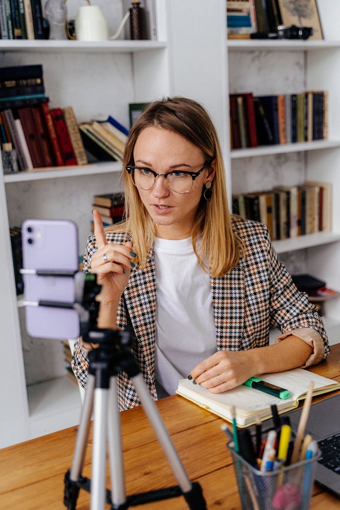 A woman in glasses delivers an online lesson using a smartphone. Modern teaching tools in a home setting.